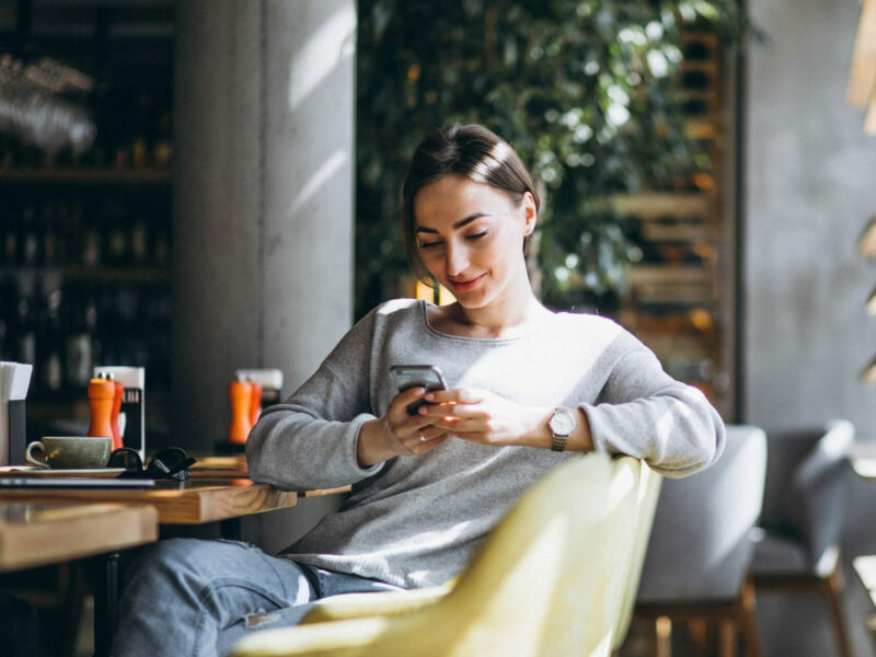 Woman sitting in a cafe drinking coffee and looking at her mobile phone